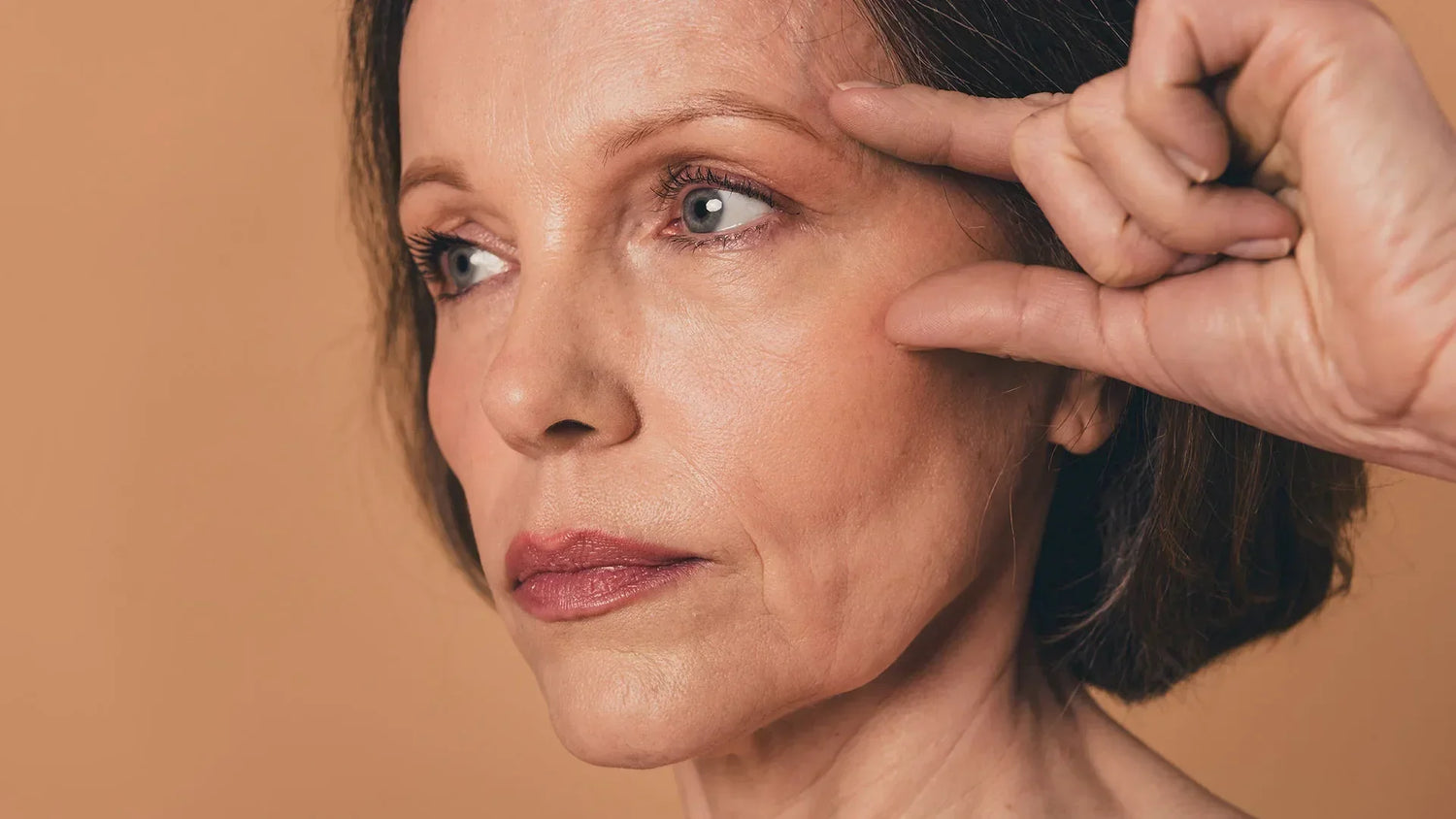 Close-up of a mature woman gently pulling the skin near her eye to illustrate a non-surgical facelift concept.